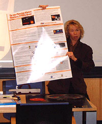 Janet Luhmann standing next to a desk, holding a poster