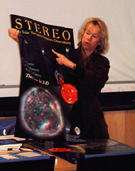 Janet Luhmann standing next to a desk holding up a poster with the Earth and the sun on it.